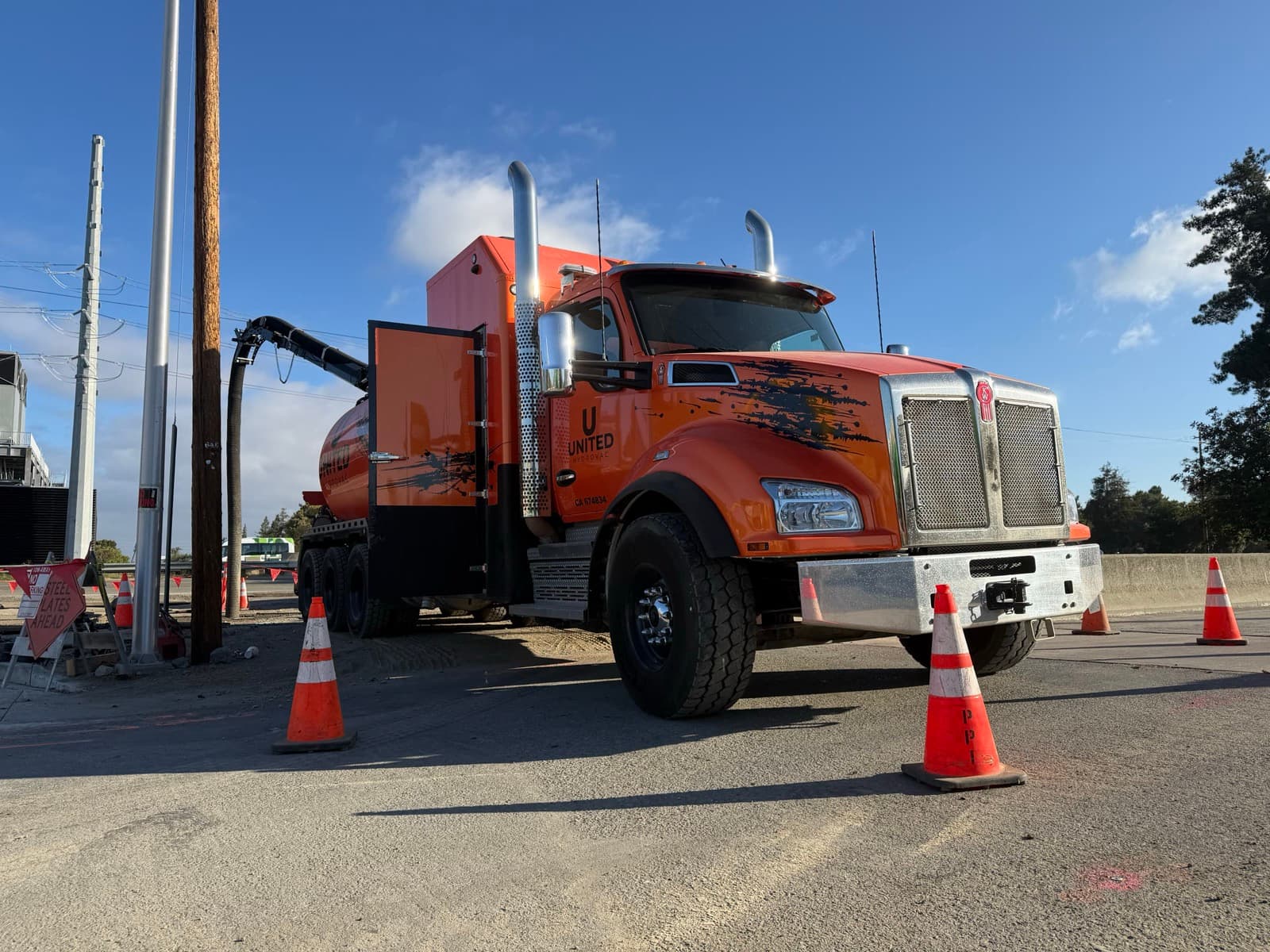 Orange United Hydrovac Kenworth vacuum truck coned off at a job site, boom lowered