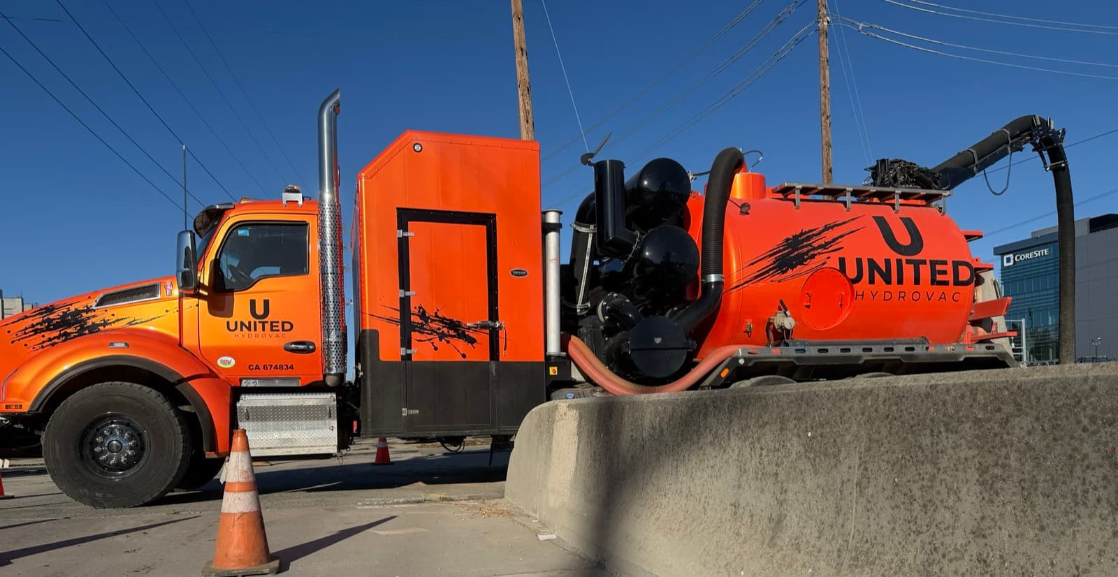Orange United Hydrovac vacuum truck in side profile, parked behind a concrete barrier