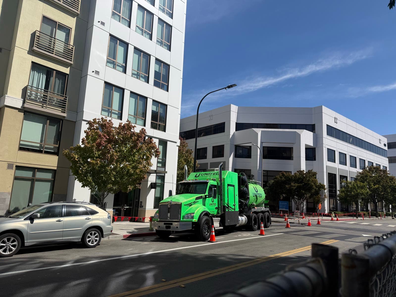 Green United Hydrovac truck working curbside on a city street, coned off between apartment and office buildings