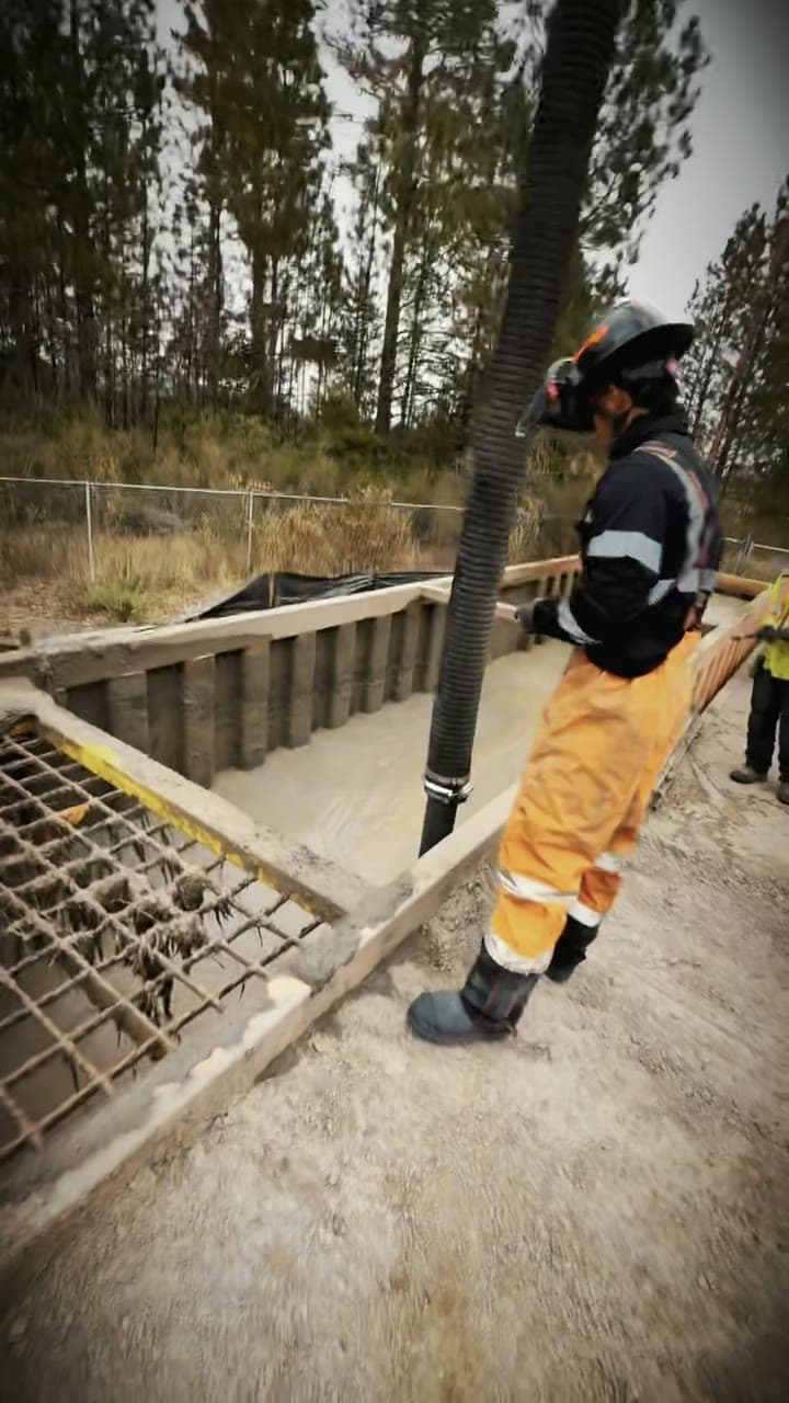 Operator in orange hi-vis guiding the vacuum hose down into a shored excavation